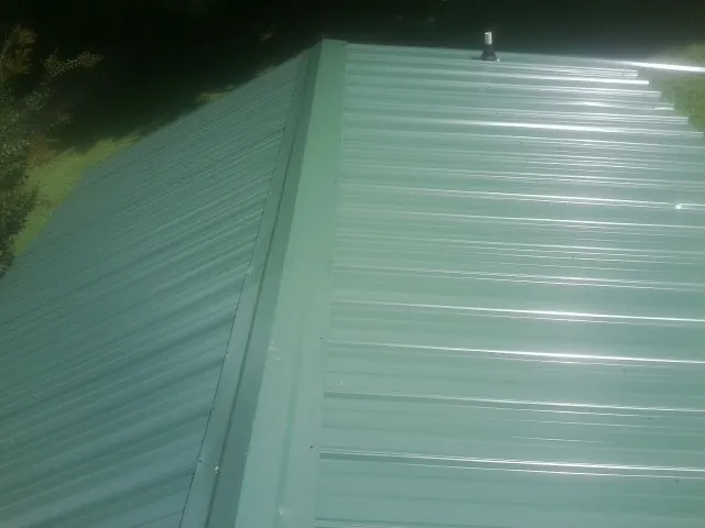 New green metal panels meeting at the ridge of a roof — Flat Roof Repair work by our crew in Magnolia